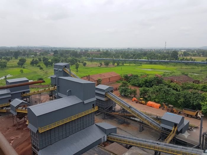 Aerial view of a processing plant with grey sheds and yellow conveyor galleries beside green fields