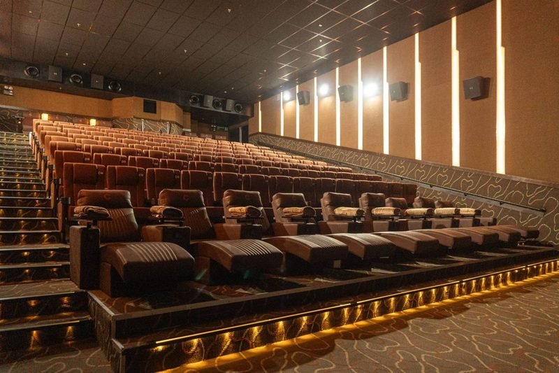 Cinèworld auditorium: rows of tan seats rising behind a front row of leather recliners with blankets, lit wall panels along the side