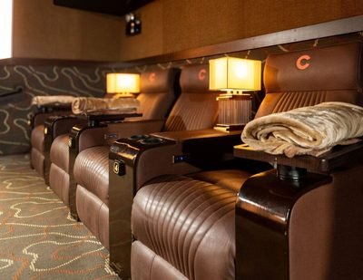 Brown leather recliners with cup holders, folded blankets and small table lamps