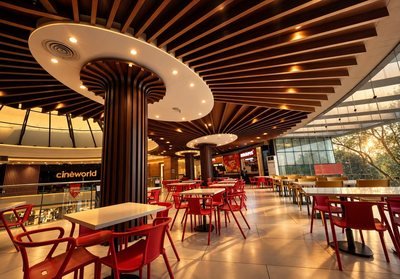 FE2 Arcade food court with red chairs under a radiating timber ceiling, glass wall and trees in evening sun